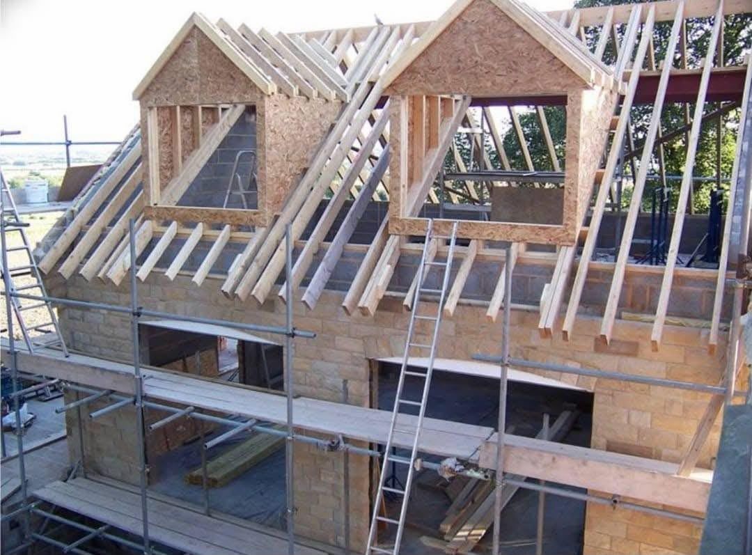 Maison en pierre sous échafaudage : charpente neuve et lucarnes montées au-dessus des murs existants