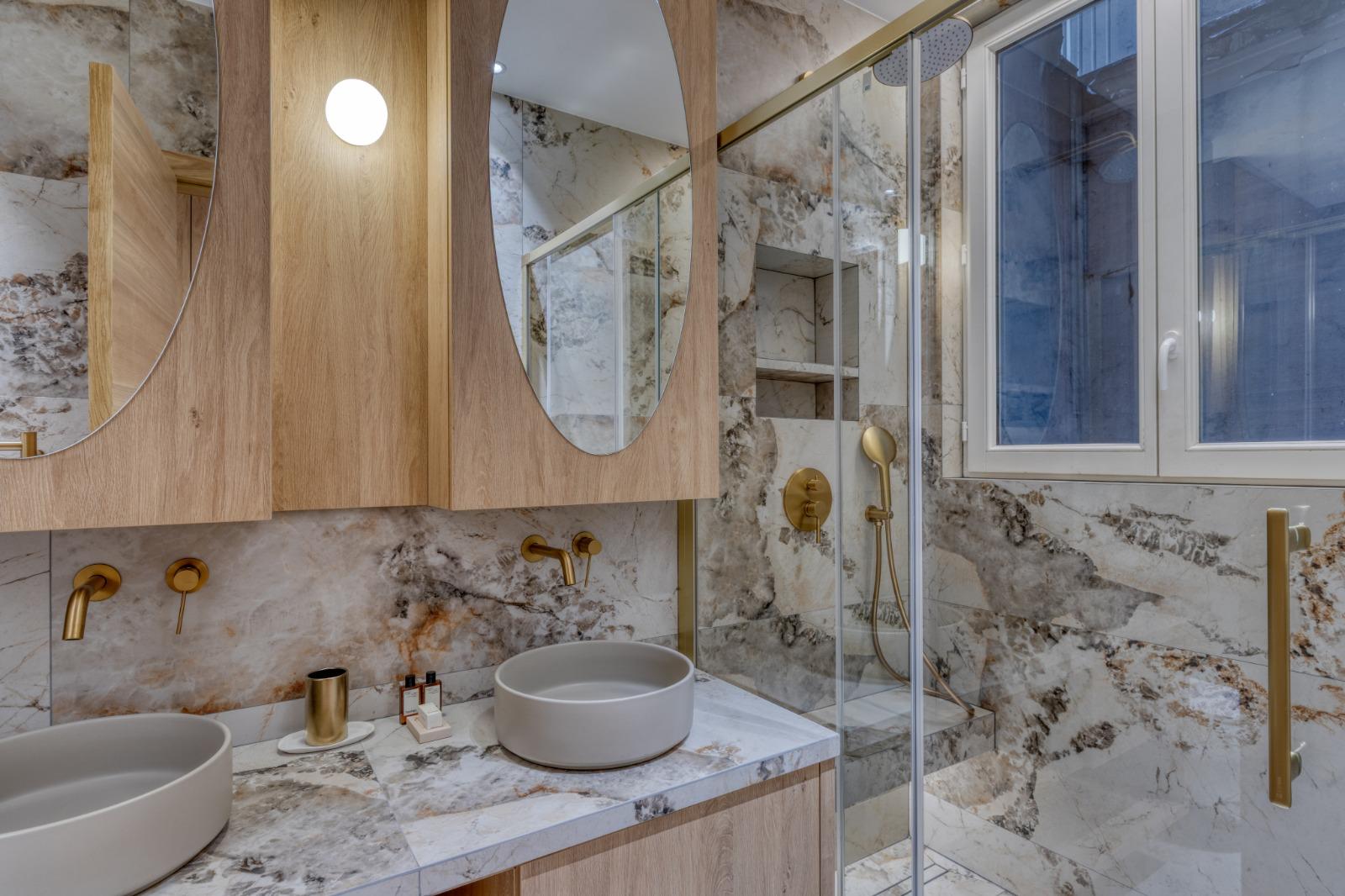Salle d'eau rénovée : double vasque sur plan en pierre veinée, miroirs ovales dans un meuble en chêne, douche vitrée